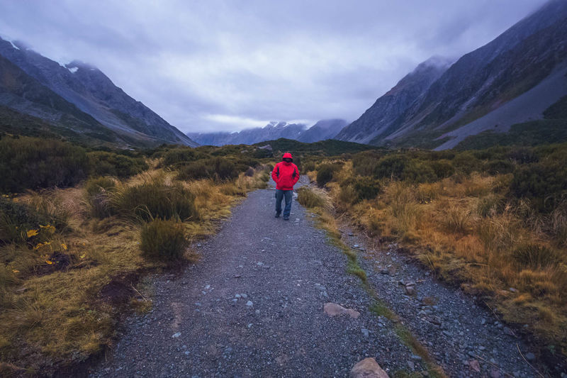 Full length of man walking on field against mountains and cloudy sky