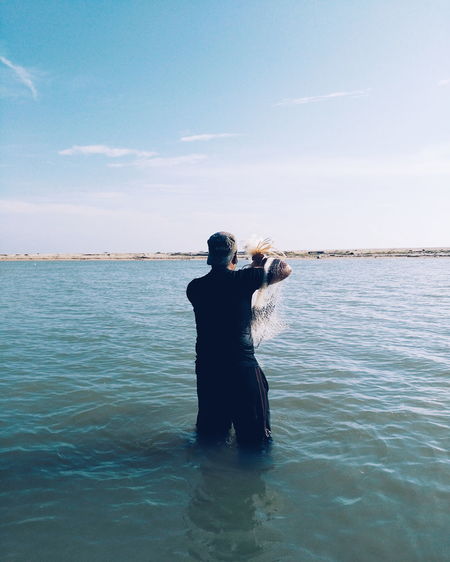 Rear view of young man standing in sea against sky