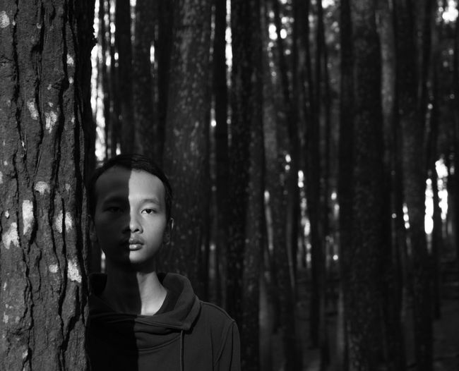 Portrait of young man standing by tree trunk in forest
