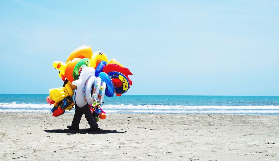 Men selling balloons on beach against clear sky