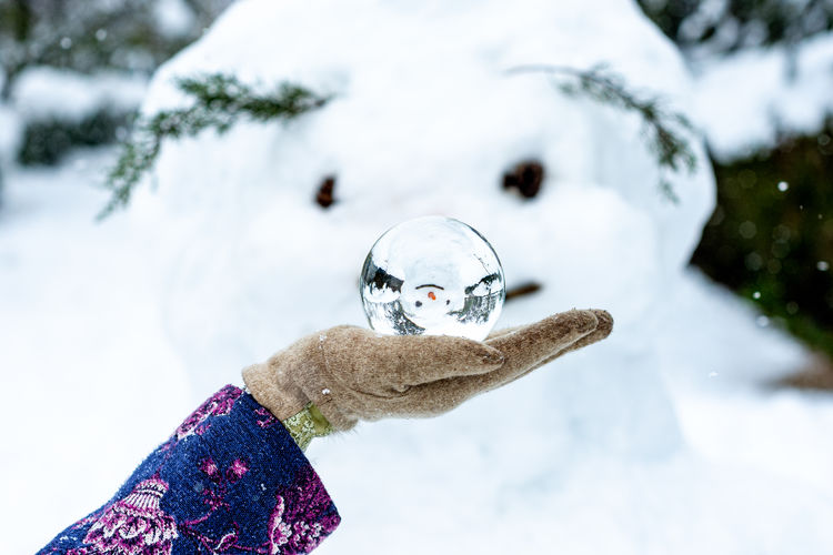 A woman's hand holding a crystal ball next to a snowman. snowy landscape on the background.