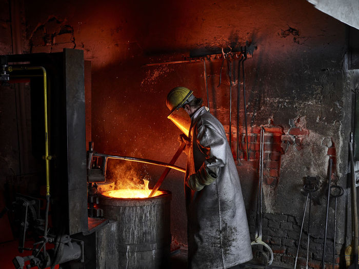 Foundry worker wearing protective suit burning in furnace at metal industry