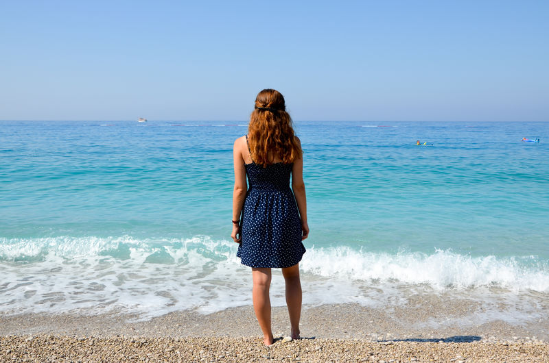 Rear view full length of woman standing on shore at beach