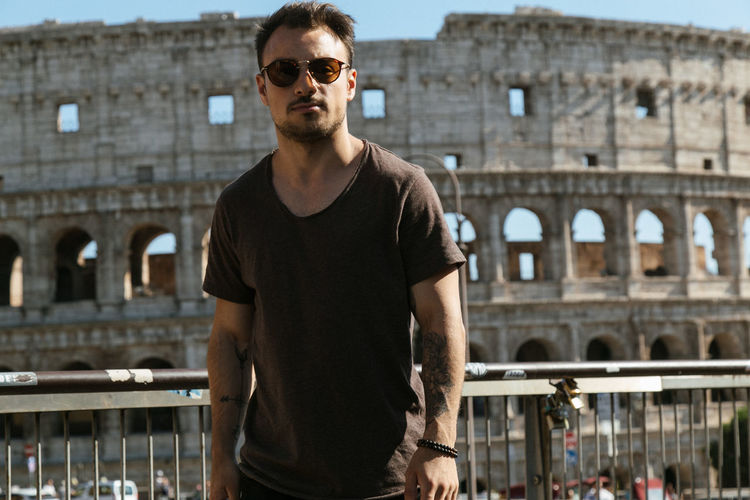 Portrait of young man wearing sunglasses while standing against coliseum