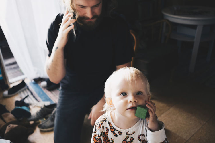 Father talking on mobile phone while girl playing with toy at home
