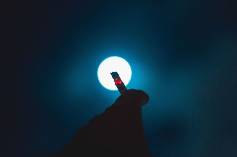 Close-up of hand holding cigarette against blue sky
