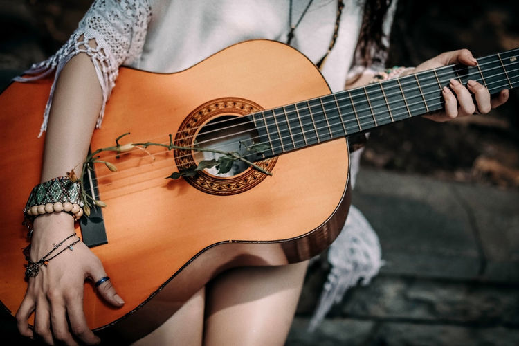 Cropped figure of hippie woman with boho wood beaded bracelets holding a guitar