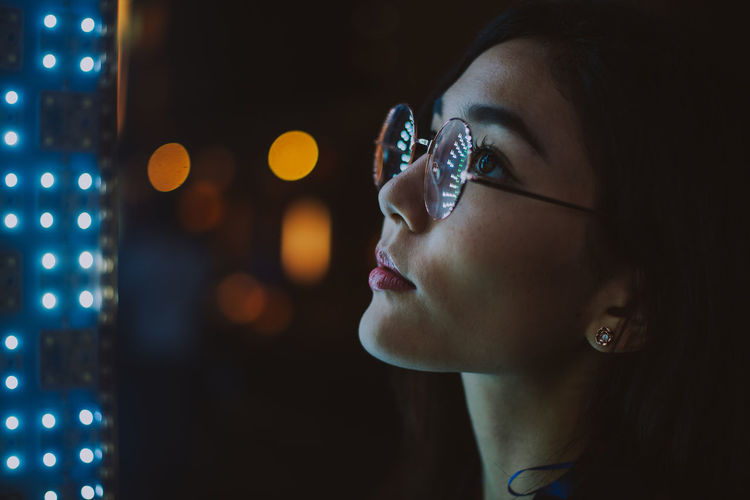 Close-up of young woman standing against illuminated city at night