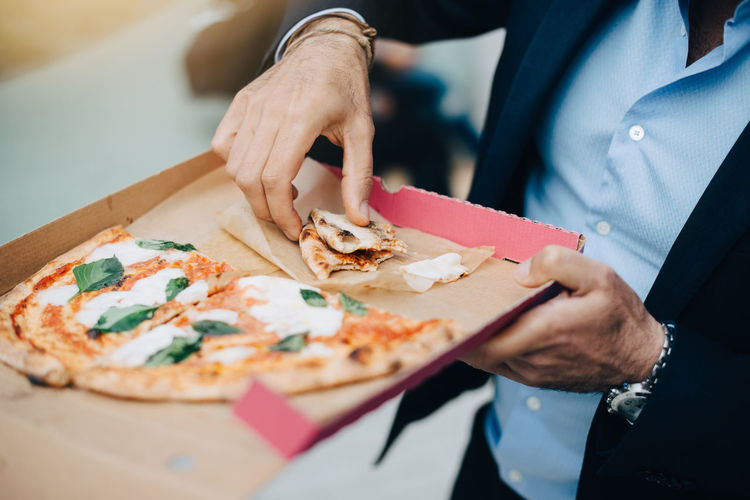 Midsection of businessman eating pizza from cardboard box in city