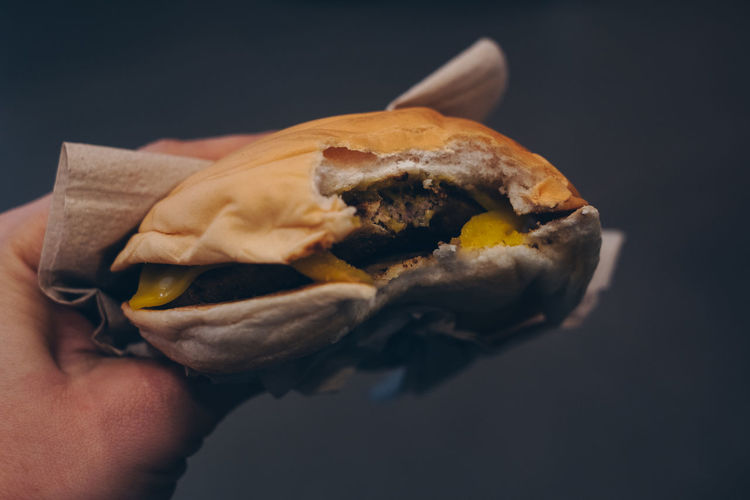 Close-up of hand holding burger against black background