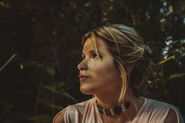 Young woman looking away against trees