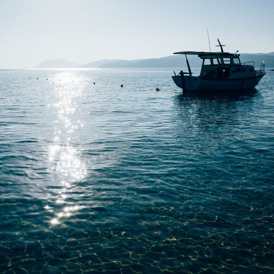 Boat sailing in sea against sky during sunny day
