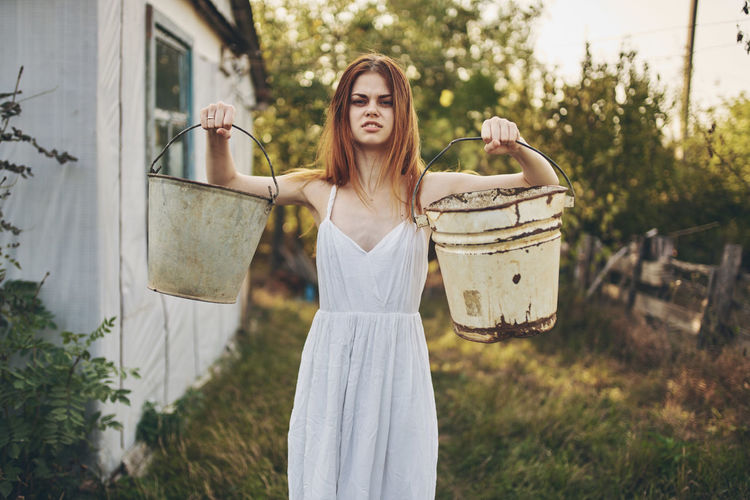 Portrait of young woman holding buckets outdoors