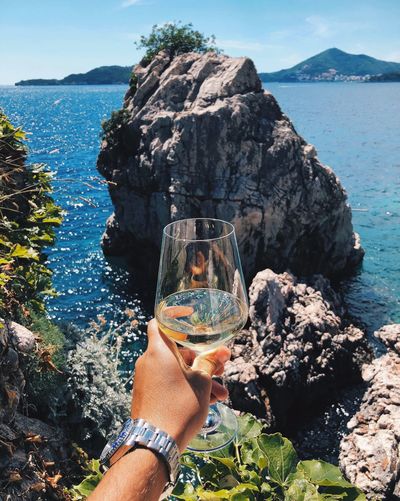 Cropped image of man holding wineglass against sea