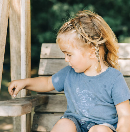 Cute girl looking away while sitting on wood