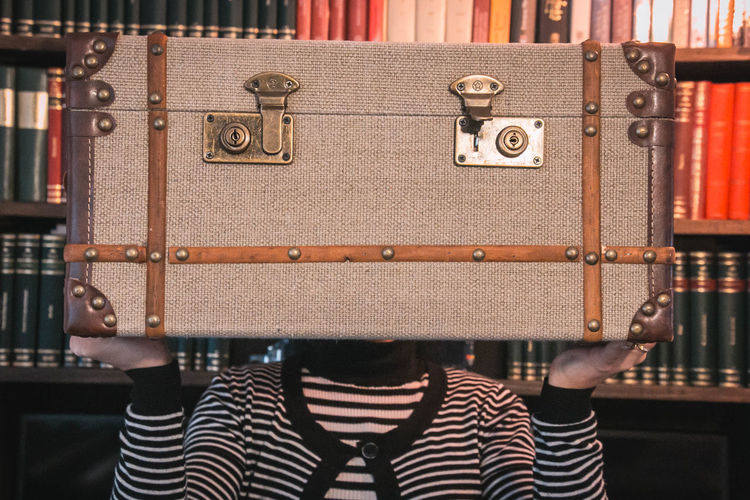 Close-up of woman holding vintage suitcase by bookshelf