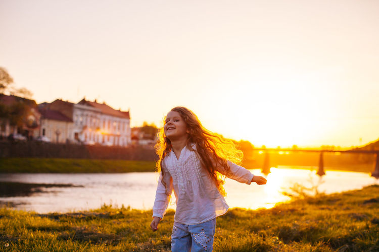 Full length of smiling young woman standing against sky during sunset