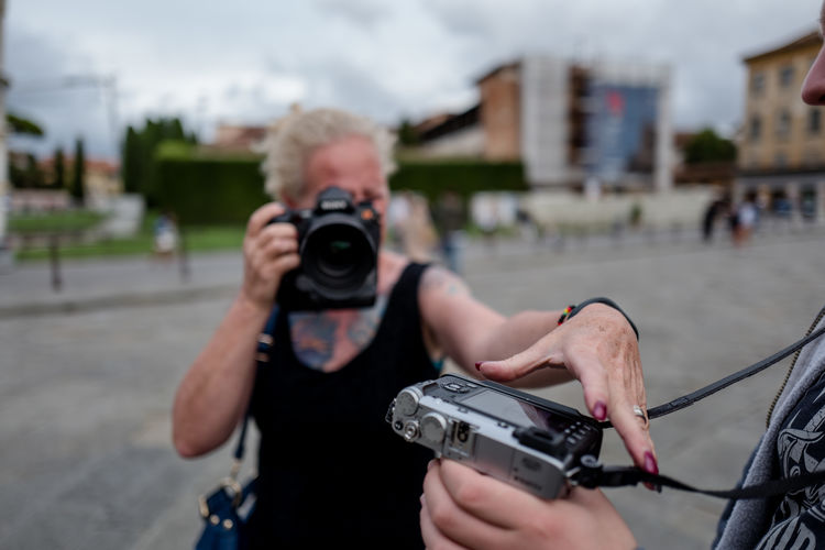 Woman photographing camera held by friend on street in city