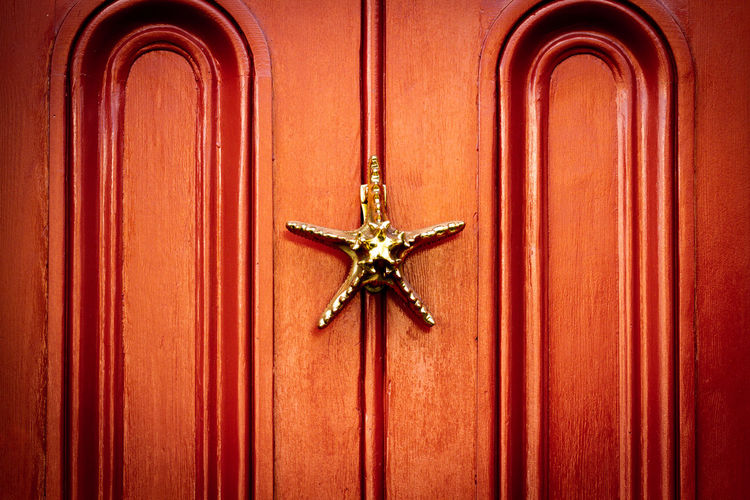 A golden starfish as a door knocker on a richly glowing wooden front door 