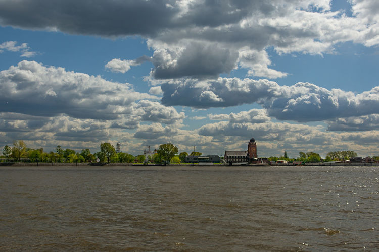 View of river by building against cloudy sky