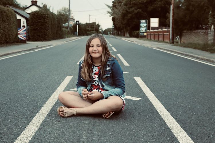 Portrait of a smiling young woman sitting on road