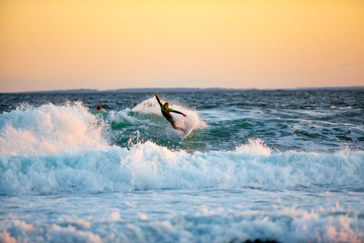 Man surfing in sea against clear sky during sunset