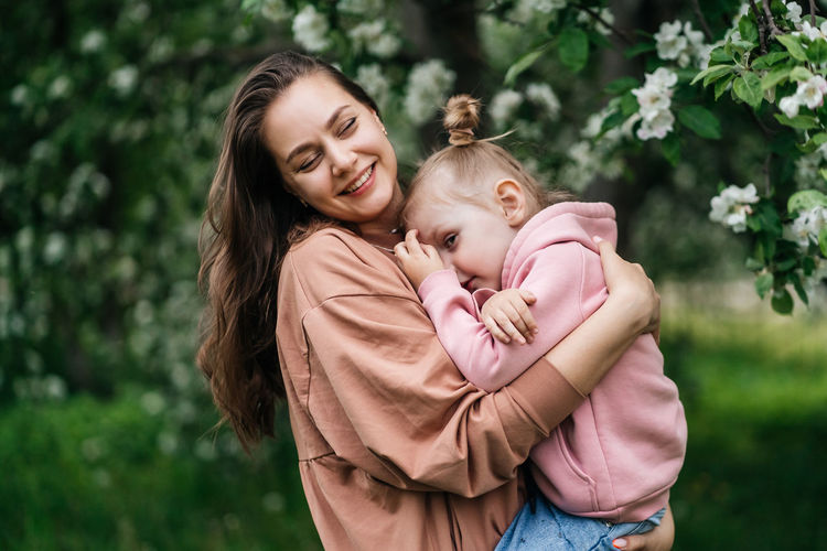 Young mother with her daughter in her arms in a blooming apple orchard