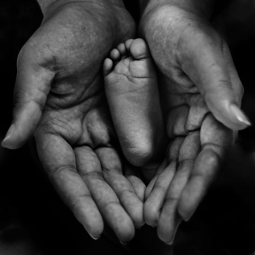 Cropped image of baby foot in woman hands against black background