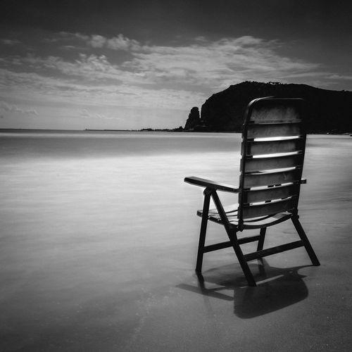 Chair on beach against sky in black and white