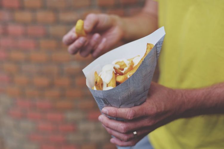 Cropped image of man holding cheesy french fries in paper cone