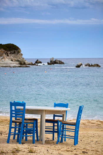 Chairs and table on beach against sky