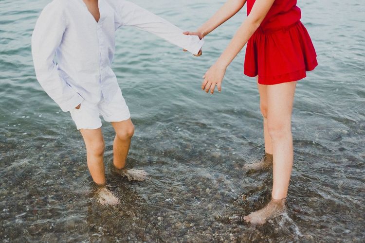 Low section of woman and boy holding hands while standing in sea