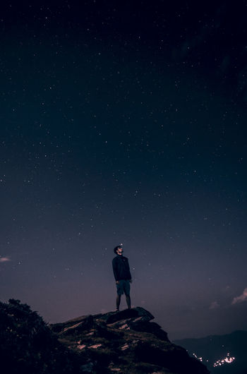 Low angle view of young man standing on cliff against star field