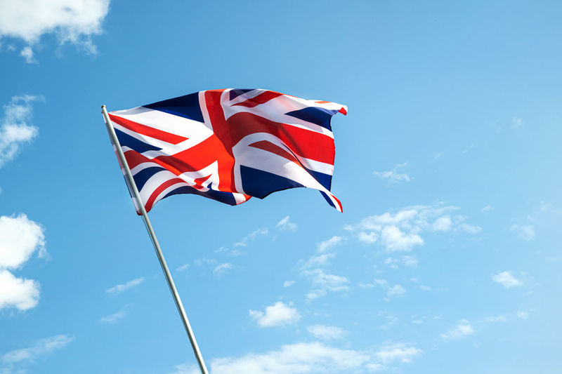 Great britain england flag waving in the wind over blue sky low angle view close up.