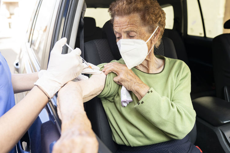 Female doctor vaccinating senior woman in car
