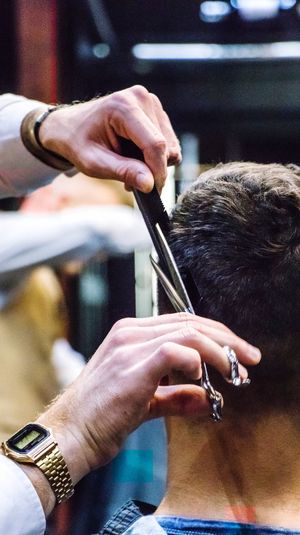 Cropped hands of barber cutting man hair in salon