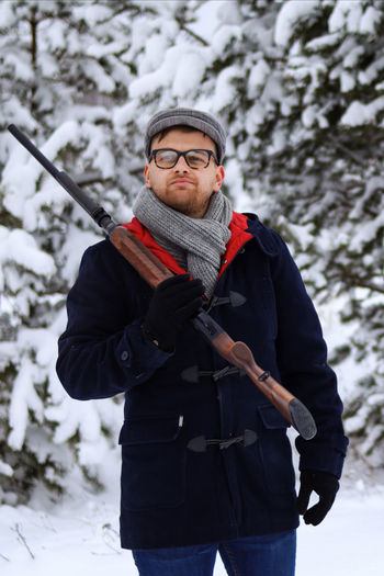 Full length of young man standing in snow with shotgun