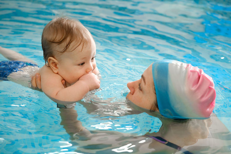 Early age swimming in pool. baby boy trained to swim in water. happy child with trainer woman in