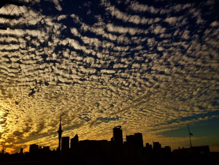 Low angle view of silhouette cityscape against cloudy sky during sunset