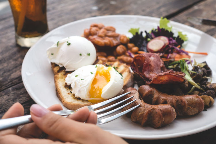 Cropped hand of person holding fork by plate on table