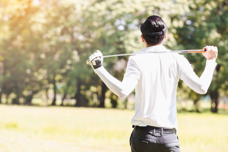 Side view of man holding golf club while standing on field