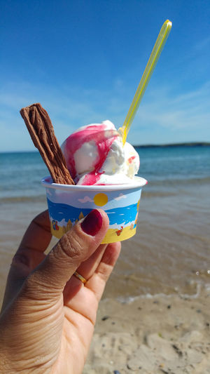 Hand holding ice cream cone at beach