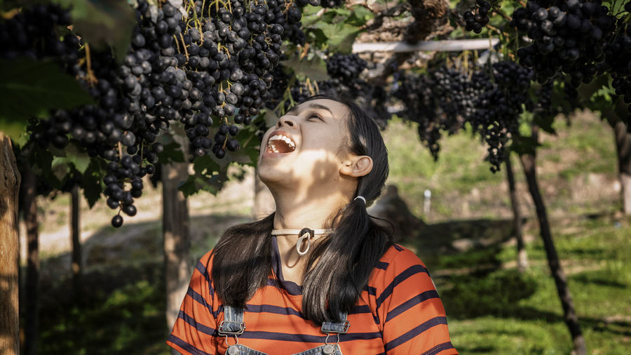 Happy  woman gardeners opened mouth with bunches of ripe grapes on vine before harvest in garden.