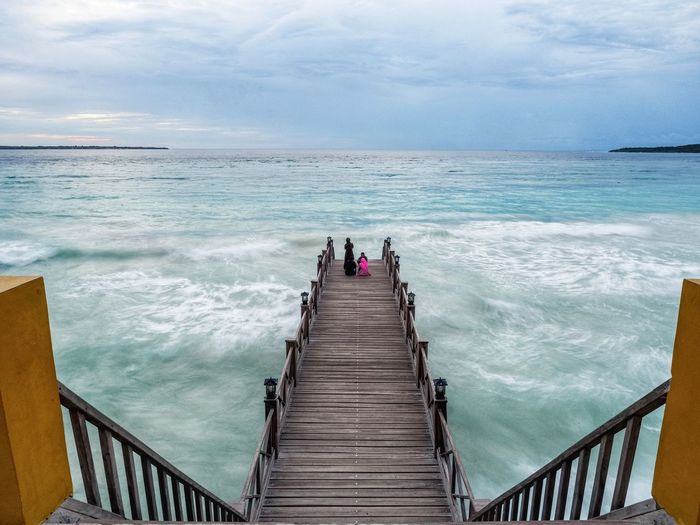 People on pier over sea against sky