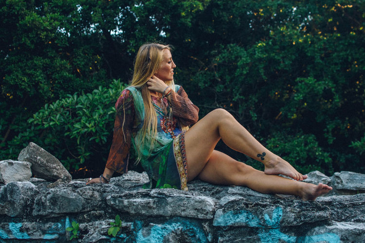 Full length of woman sitting on stone wall outdoors