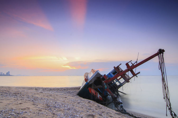Abandoned ship on beach against sky during sunset