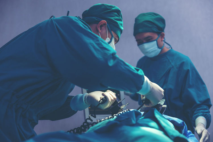 While performing medical surgery inside the operating room, a doctor and nurse use a defibrillator.