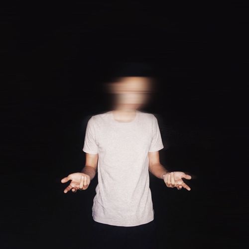 Man with blurry face standing against black background