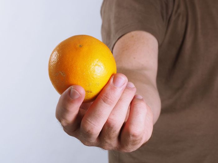 Close-up of hand holding fruit against white background