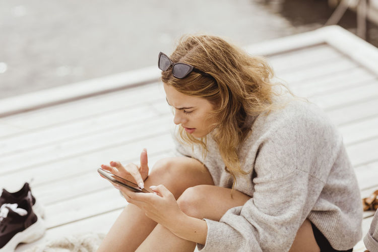 Blond woman using smart phone while sitting on jetty